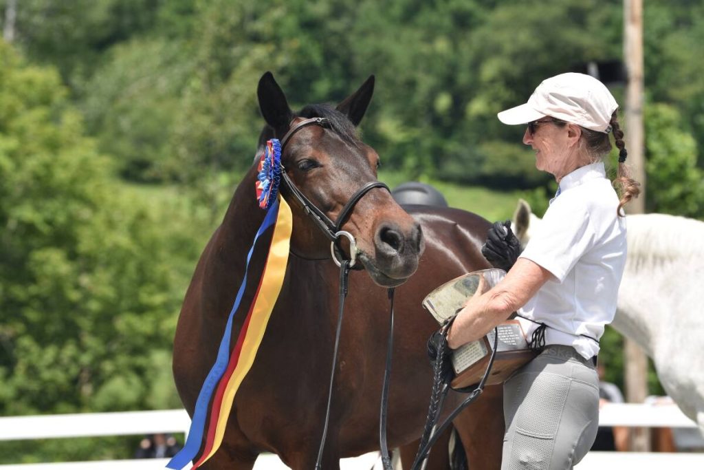 horse with ribbon on brdile next to handler with trophy