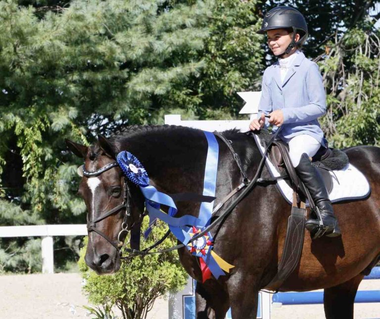 Girl in blue coat riding pony with blue ribbon
